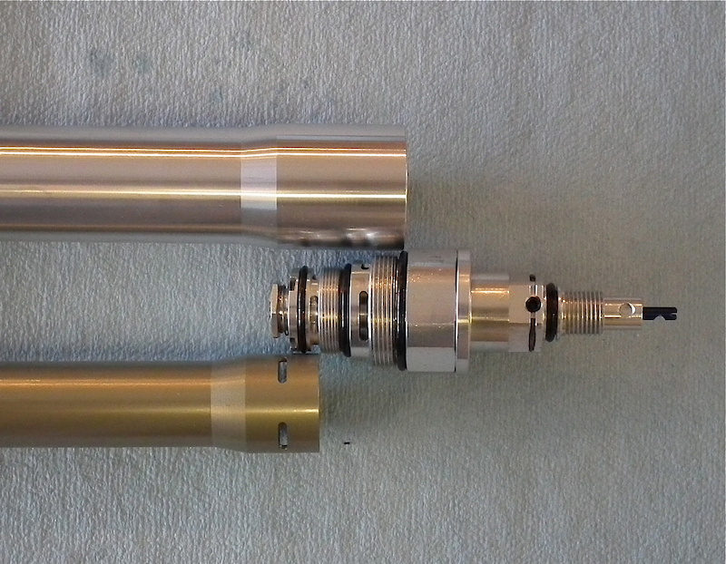 Those trick looking anodized aluminum knobs at the bottom of the fork are attached to this CNC'd piece of hardware that controls the separate high and low speed compression duties of the HLR and allows you to tune each one independently of one another. The blue dial (low speed compression) is attached to the black adjuster on the far right of the unit. Turning this dictates oil flow during low speed compression action, such as braking, body movement, and smoother landings. Turning it to the right adds damping and you'll find that the fork will use less travel during these instances, turning it to the left has the opposite effect. High speed compression is adjusted via the gold knob that is attached to the silver section just above this, you can see where the setscrew tightens against it. Extra high speed compression will keep the Vengeance from using too much travel during hard hits. This photo also clearly shows the oil ports in the damper tube in relation to the ports on the compression assembly.