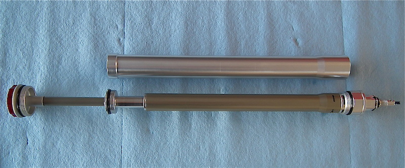 You're looking at the sealed, but serviceable, twin tube damper cartridge that is housed in the right leg of the Vengeance. The larger diameter silver tube encompasses the damping cartridge and completely separates lube and damping oil from one another. This not only keeps cavitation to a minimum due to the system preventing the oil from sloshing about inside the fork, but it also eliminates the chance of dirt and grime that has managed to get past the seals from mixing in with the damping oil. There is also less oil needed within the fork to perform damping duties, thereby lower weight as well. Under compression, the oil runs through the compression damping circuits that are located at the bottom of the cartridge and then out the ports into the outer chamber that is created by the silver tube. The opposite happens during the rebound stroke, with the oil flowing in through the ports, past the check valve, and through the rebound assembly.
