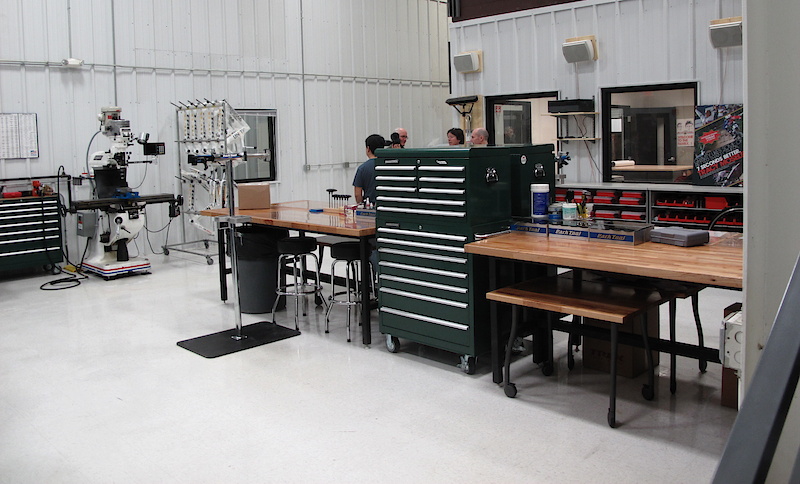<span style='font-size:18px'>Trek's Race Shop</span><br><br>We can only imagine the rad race-team-only products that have made their way through this spotless room. I challenge anyone to find a spec of dust or dirt in here, it is kept clean to a nearly surgical room kind of level. Team rider's gear gets the special treatment in here, be it a completely custom made gadget on the in-house CNC machine or one-off frames like McCaul's slopestyle bike. Hanging on the rack up against the far wall is a selection of frames bound for Trek's professional road team, including their impressive carbon time trial rig. There is a Park Tool for any sort of repair that would ever need to be done, and the work benches use massive solid wood table tops. This room can get quite loud when machines are being used so they have pimped it out with a monster sized JBL stereo system. To all home mechanics out there, you can close your mouth now.