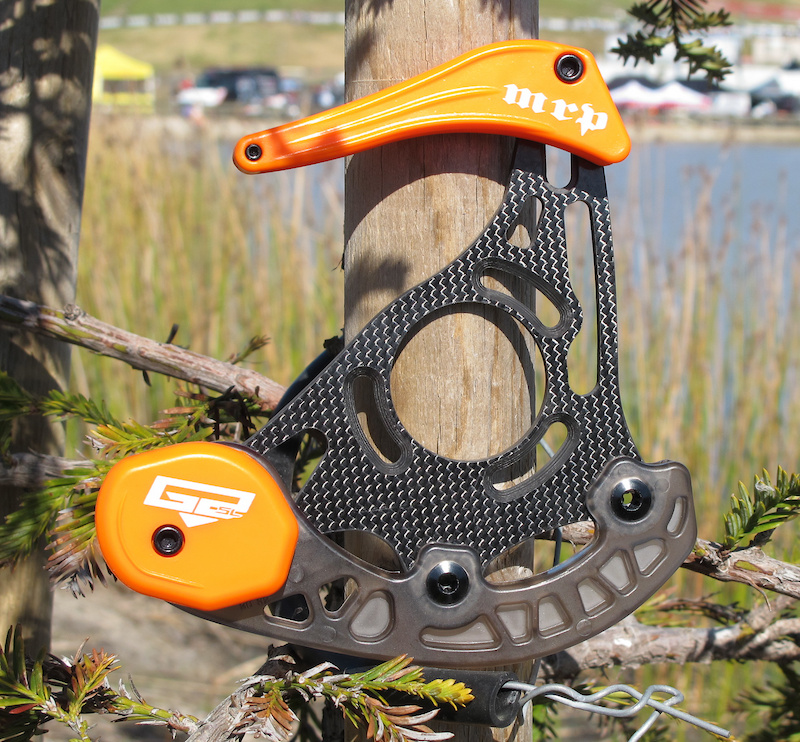 MRP has taken their popular and easy to install G2 guide and added carbon to the mix. The new carbon back plate is not just for light weight, but also for resiliency - MRP says that the carbon back plate is far more likely to spring back to its original position after an impact, whereas the aluminum version may bend and stay in place. It also doesn't hurt that the G2 Carbon is also 35 grams lighter than the standard G2.<br><br><span style='font-size:19px'>MRP G2 Carbon details:</span><br><br>- Carbon back plate<br>- Integrated and replaceable skid plate design<br>- Sealed bearing pulley wheel protected in skid plate<br>- Front-access, single-bolt positioning of upper and lower guide<br>- Captive hardware<br>- Fits 32-36 and 36-40 tooth rings<br>- Weight: 140 grams (<i>approx</i>)<br>- Price: TBA