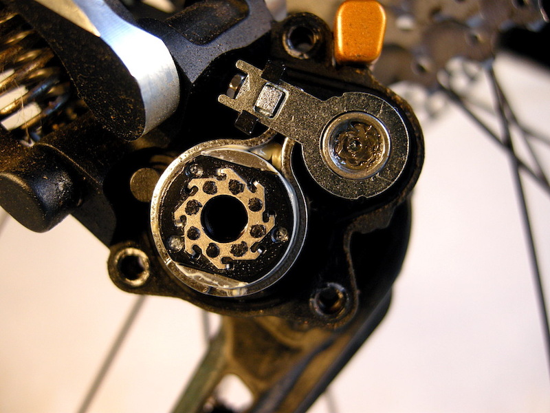 The one-way roller clutch is the larger cylinder at the lower left. The stainless steel band that encircles it is the friction brake. The adjustment wrench is stowed in the housing above the clutch. The friction adjustment nut is visible in the hex end of the tiny wrench.