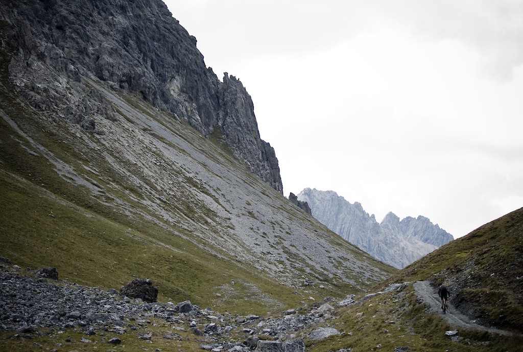 <span style='font-size:12px'>Each climb out of one valley delivered a change of scenery, like the Trela Pass out of Livigno. Tours are like that: a never ending supply of visual rewards, with the well earned feeling of accomplishment remote passes like this can deliver.</span><br><br>The Bernina Pass often acts as a barrier to storms, but the rain that we wake to in Poschiavo is still with us as we jump from the train back at the pass, clad head to foot in wet weather gear, to set off along a rumble-strip of slippery rocks that tests our technical prowess. Thankfully the rain eases off as we start a 1200 ft climb up the Val de Fain valley toward the La Stretta pass from where we will ride down into Italy. 'So where is the trail?' Guillaume asks when we reach the lofty pass. We're shrouded in mist but through the murkiness I can make out the edge of an abyss: the trail appears to literally drop off the edge of the world. The exposure renders the initial descent a hike-a-bike and in places we have to hang onto chains anchored into the rock. I start to get the feeling that the Alta Rezia is not only about the bike parks of Livigno, but about adventure biking in the purest sense of the term. It's a buzz though, and despite the weather the adventure factor kicks in to make it one of the most memorable days of a summer of riding. The rain returns as we ride a dozen tight switchbacks before spinning the final fast kilometres of open trail to the warm and comfy Baita Montana Hotel in Livigno.